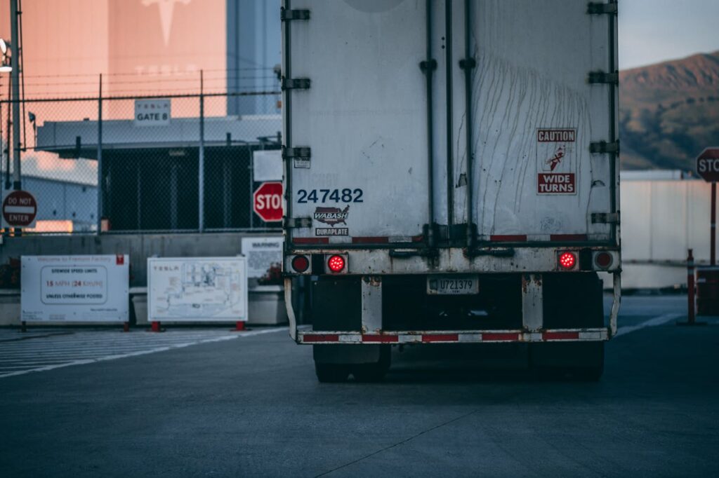 Semi truck parked at a loading dock with visible caution signs and industrial surroundings.