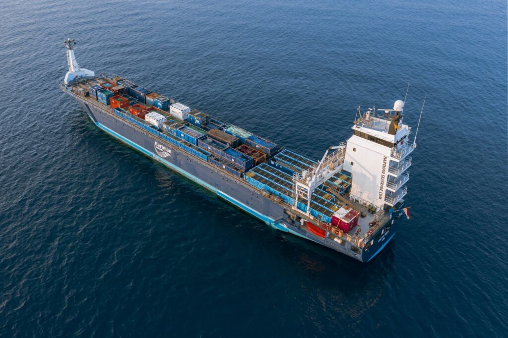 A drone captures a vibrant container ship navigating deep blue ocean waters.