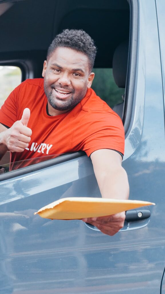 Smiling delivery man handing out a package from a van window, showcasing friendly service.